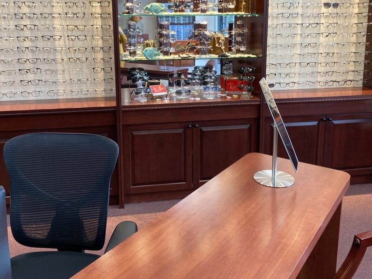 A well-organized eyeglass store display featuring shelves filled with various glasses frames, a counter with a sleek stand, and a chair in the foreground - Yucaipa Optometry Interior of a Yucaipa Optometry office showing a stylish eyewear display and consultation desk.